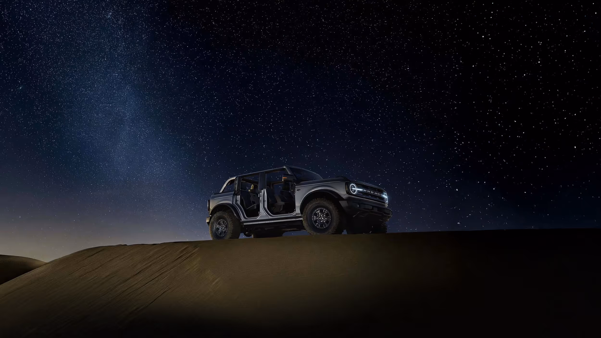Ford Bronco parked under starry night sky on desert ridge.