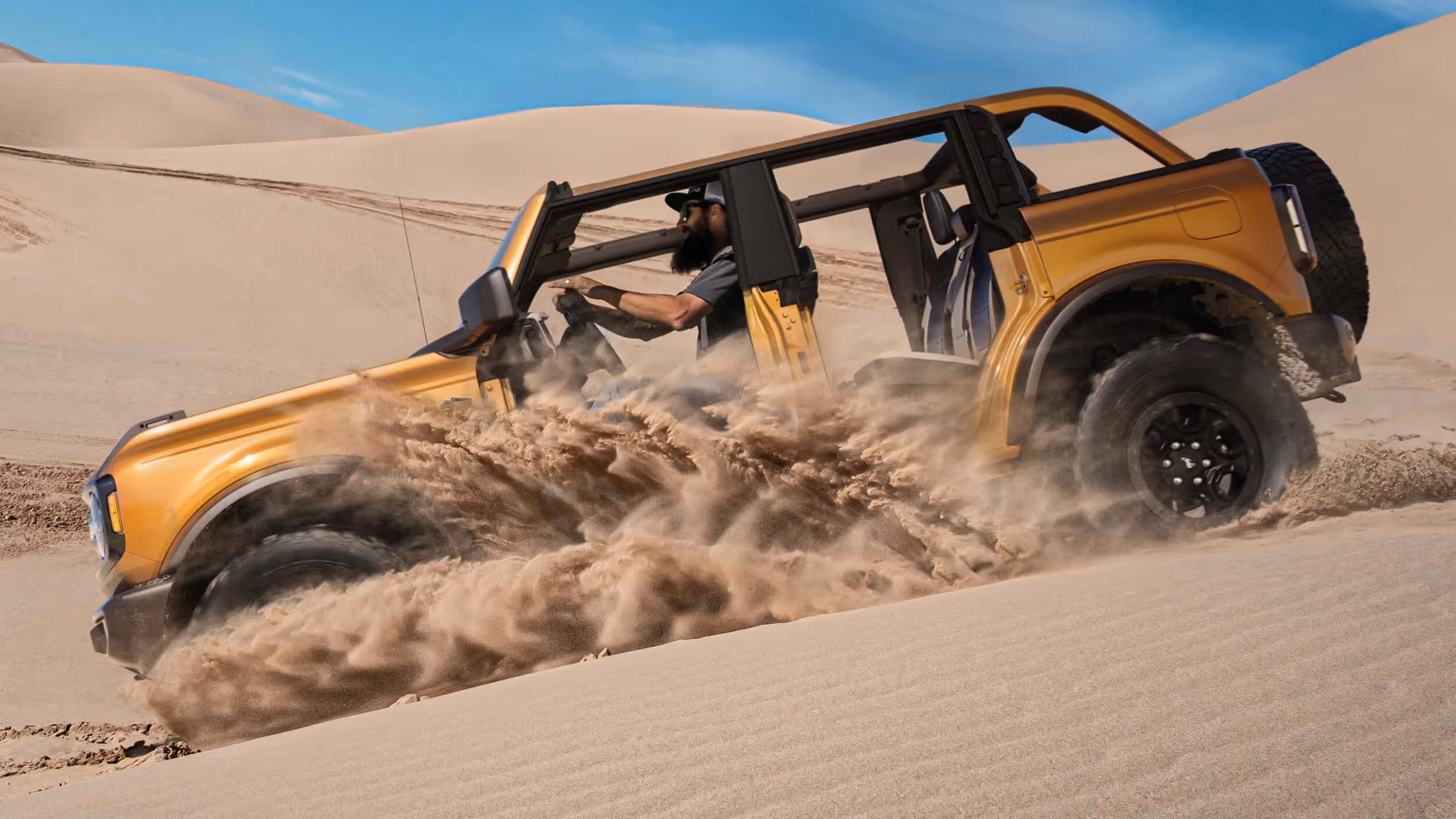 Yellow Ford Bronco kicking up sand while carving through dunes.