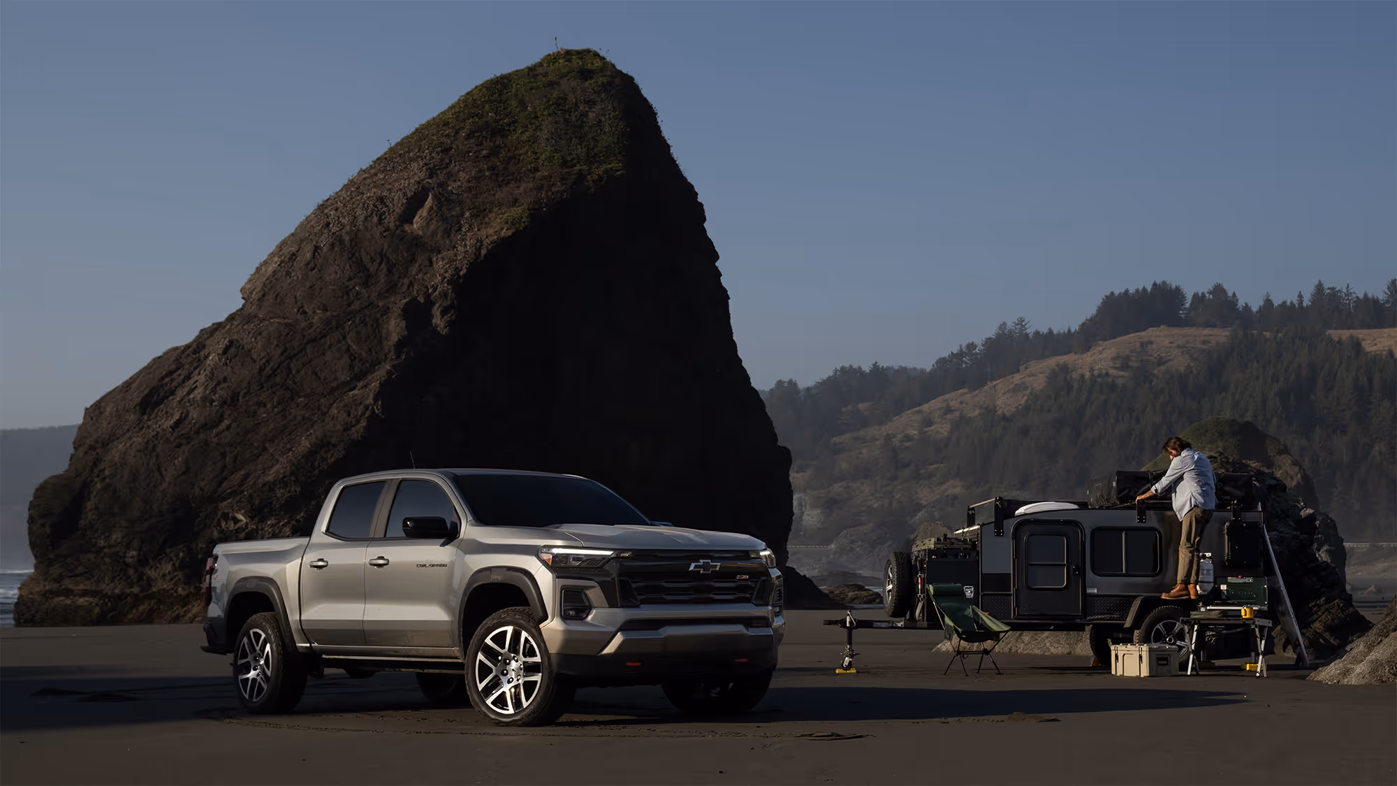Chevrolet Colorado ZR2 parked beside an overland trailer on a rugged beach with large sea stack rock formation