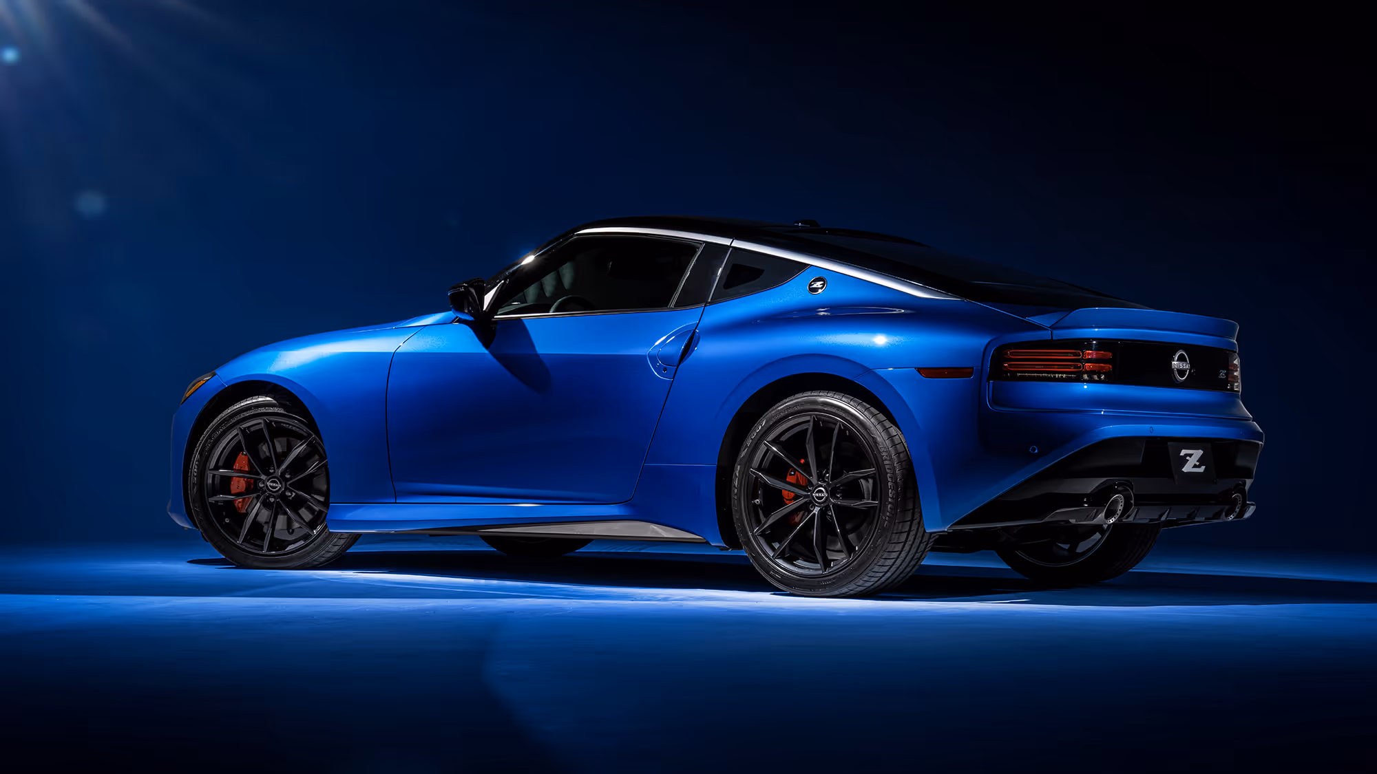 Rear three-quarter view of a blue Nissan Z sports car in a studio setting with dramatic lighting and deep blue background