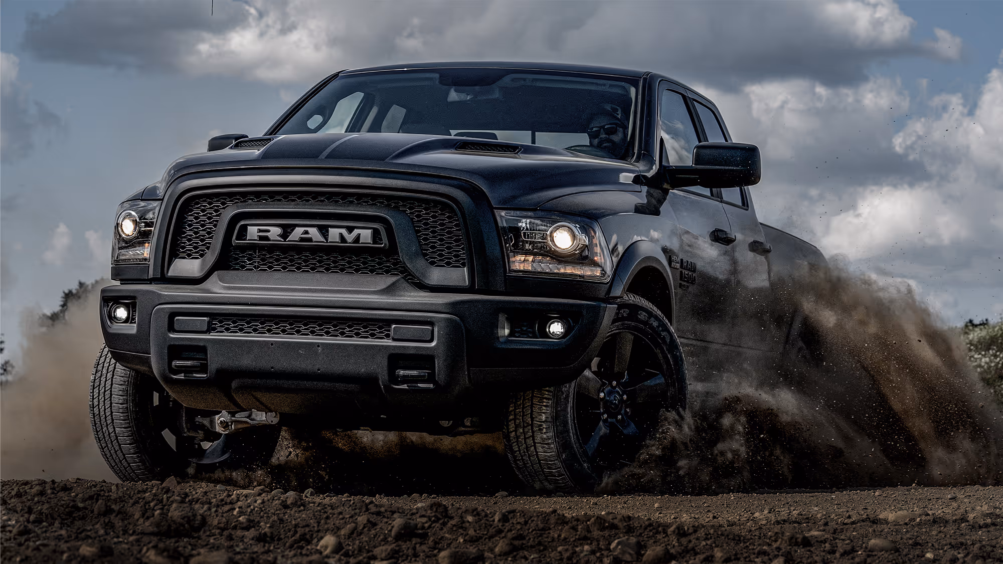 Black RAM truck driving through dirt terrain, kicking up dust to showcase power, performance, and off-road confidence.