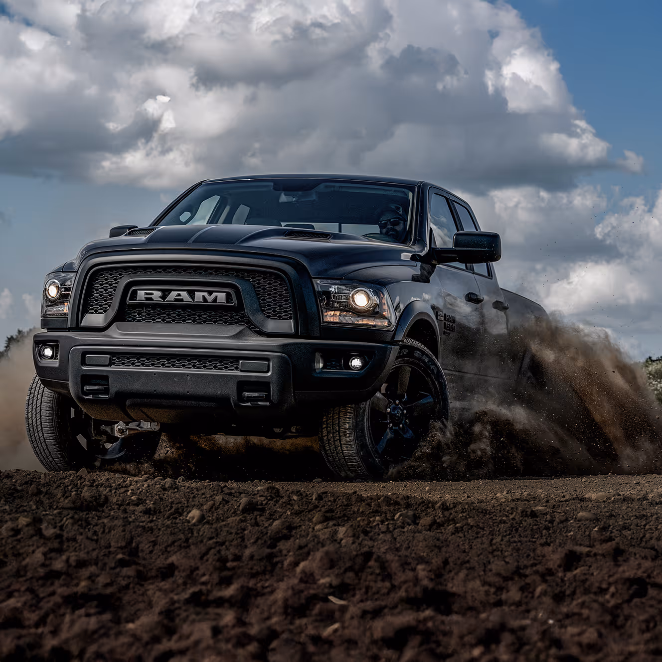 Black RAM truck driving through dirt terrain, kicking up dust to showcase power, performance, and off-road confidence.