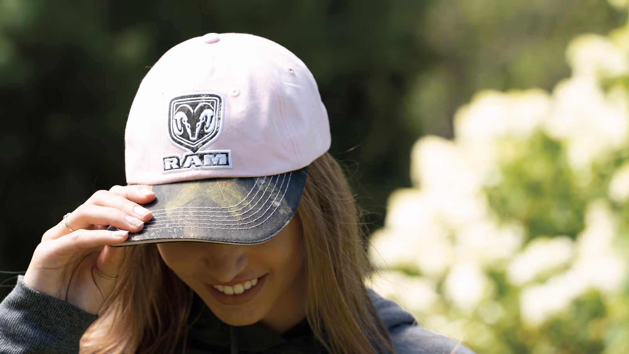Person adjusting a RAM-branded cap outdoors, capturing lifestyle and brand connection in natural light.