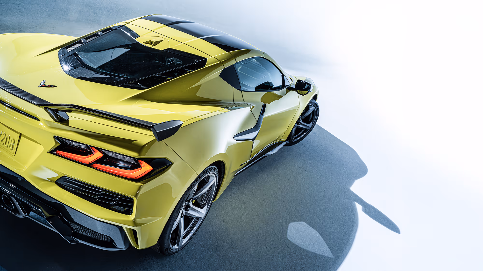 Overhead rear three-quarter view of yellow Corvette Z06 in studio, showcasing full form, stance, and aerodynamic features.