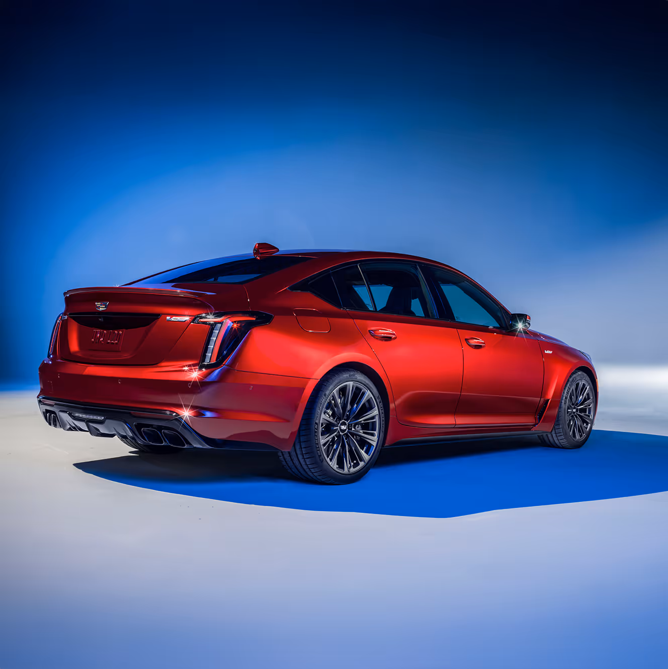 Red Cadillac CT5-V Blackwing rear three-quarter view in studio with blue gradient background and crisp rim lighting.