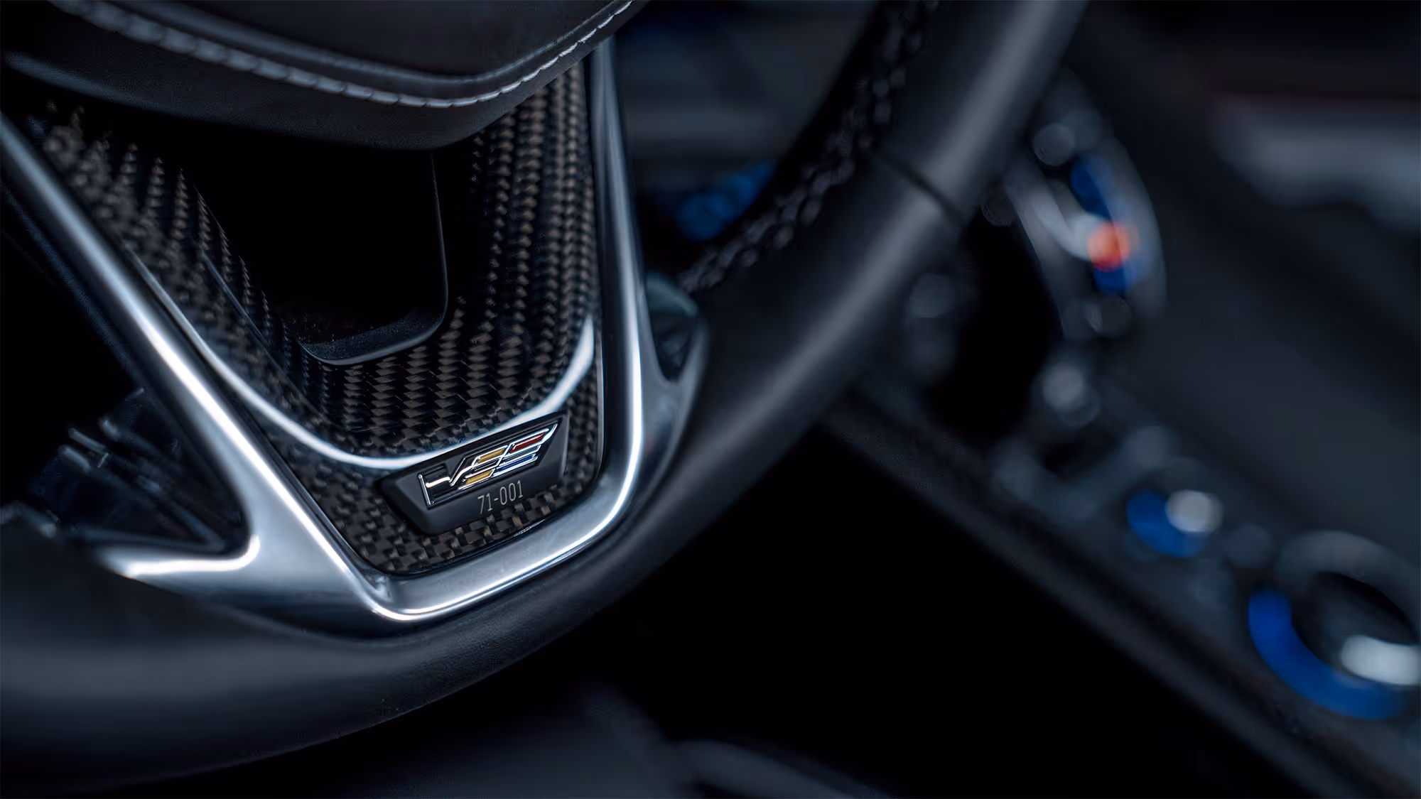 Carbon fiber interior trim detail with V-Series badge and shallow depth of field.
