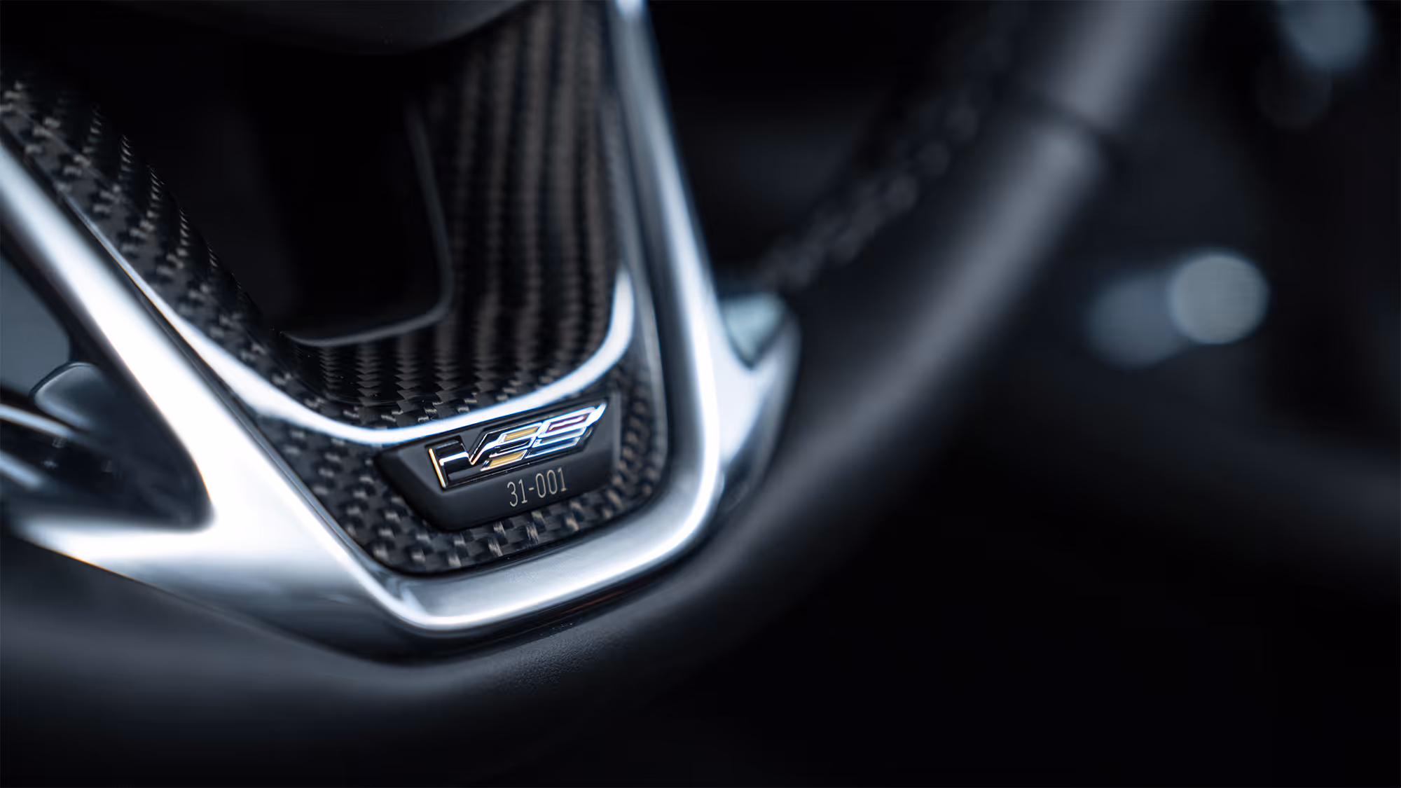 Carbon fiber interior trim detail with V-Series badge and shallow depth of field.