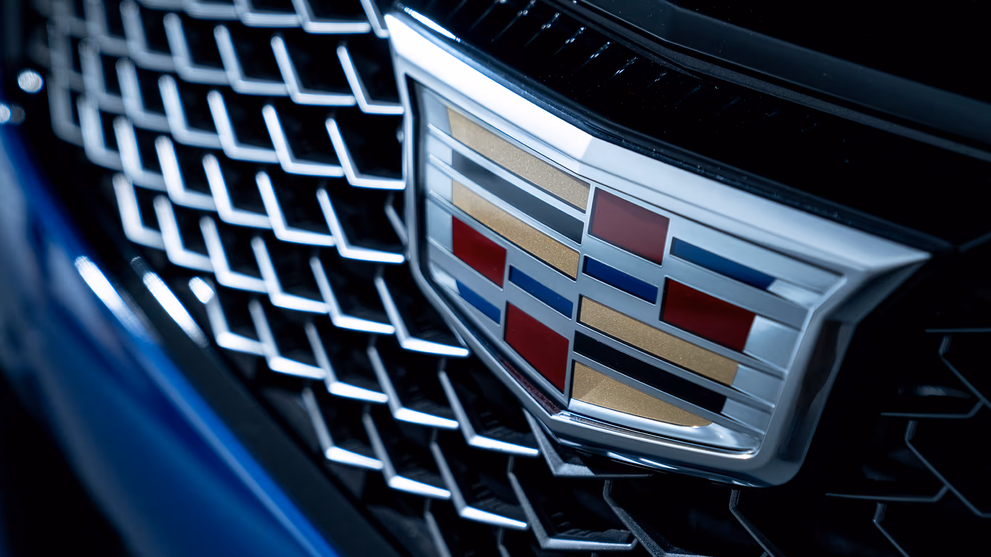 Close-up of Cadillac crest on front grille with geometric mesh pattern.