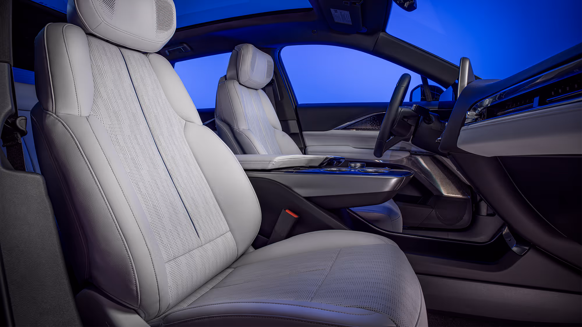 Front interior view of Cadillac LYRIQ featuring light-colored leather seats, center console, and ambient blue lighting.