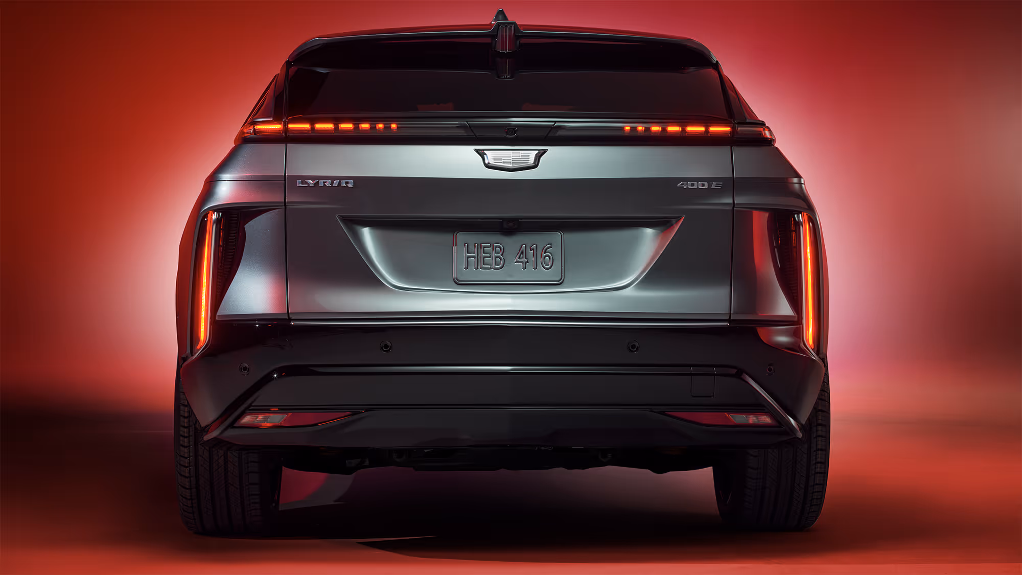 Rear view of Cadillac LYRIQ with illuminated LED taillights and centered badge, set against a red studio backdrop.