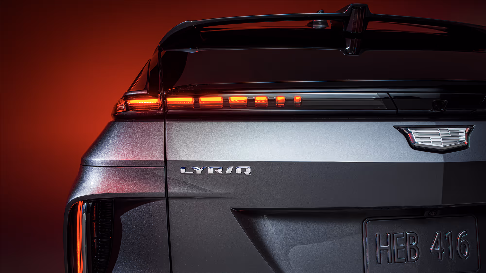 Rear three-quarter close-up of Cadillac LYRIQ showing taillight detail, badge, and sculpted tailgate on a red background.