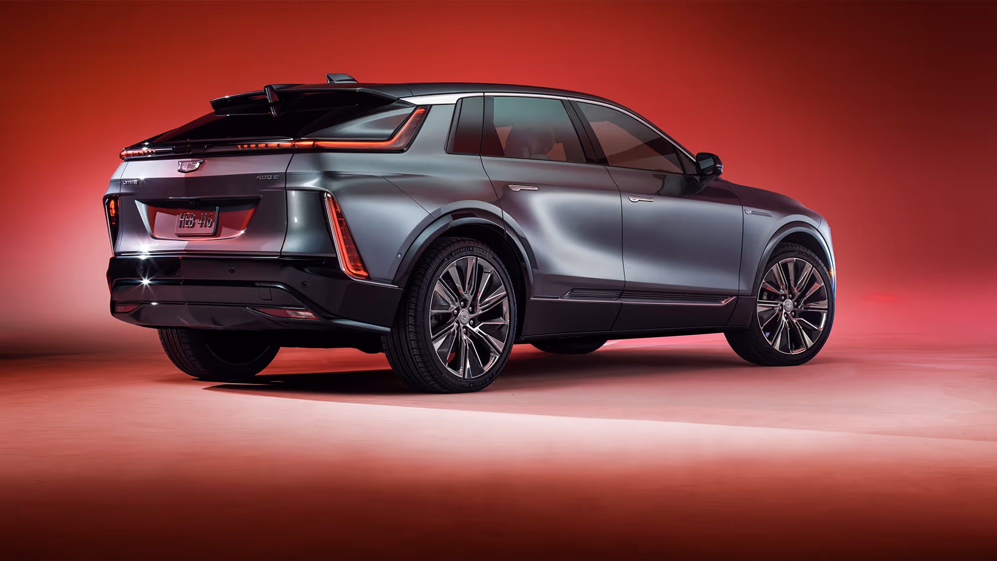 Rear three-quarter view of Cadillac LYRIQ highlighting sculpted body, LED taillights, and wheel design on a red studio backdrop.