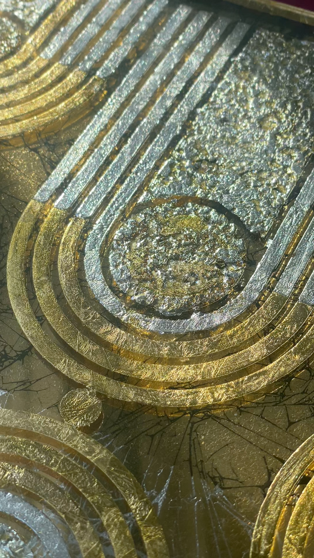 Close-up of a textured metallic surface with circular and linear gold and silver patterns and cracks.
