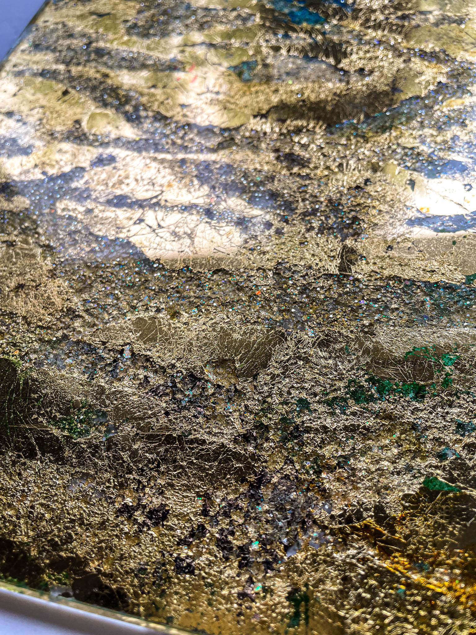 Close-up of a textured surface with cracked gold leaf and small sparkling blue and green specks.