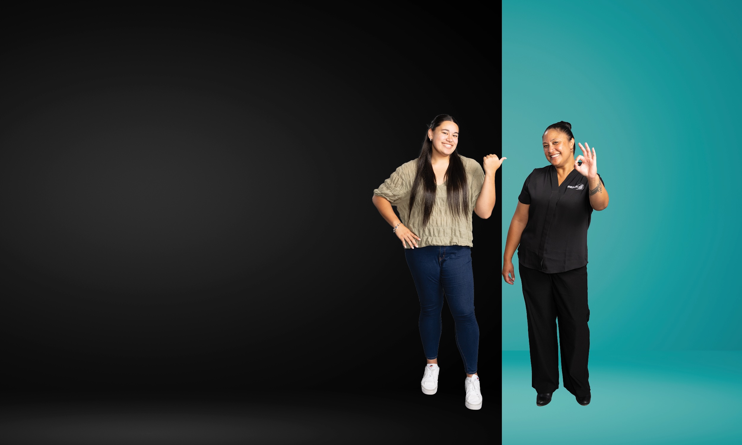 Two smiling women standing against a split background, one on a black side pointing thumb at the other, who on a teal side shows an OK hand gesture.