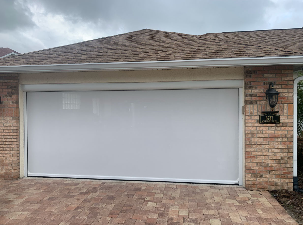 Motorized retractable garage door screen lowered on a brick home with paver driveway