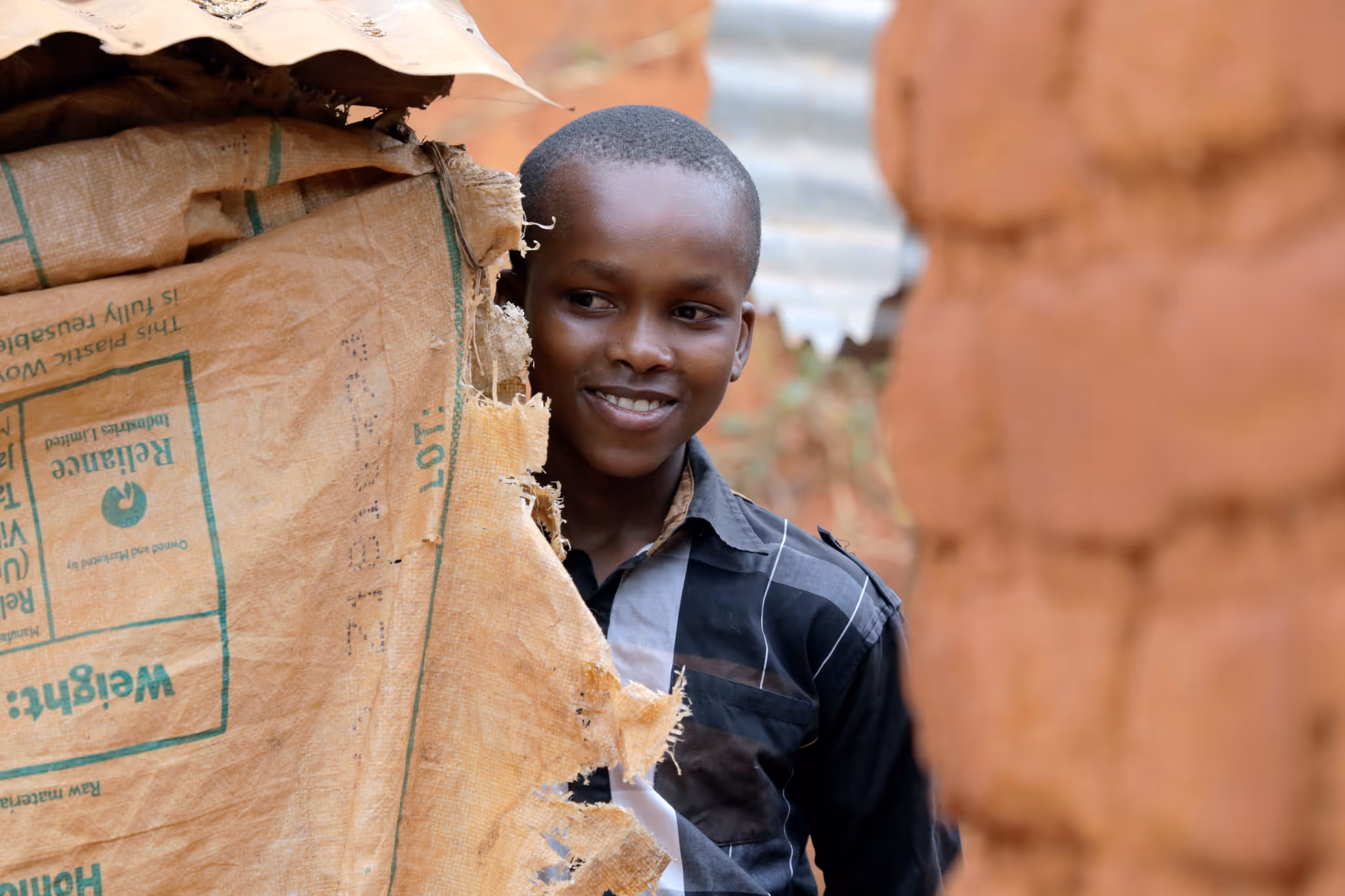 Boy playing with a string game on his hands outdoors with another child blurred in the background.