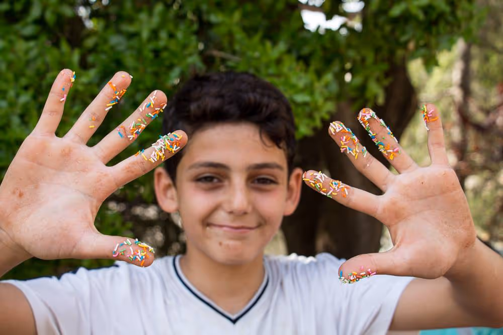 Three smiling children sitting outdoors, holding colorful cups and drinking.