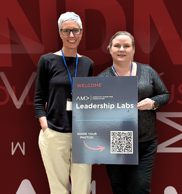 Two women standing and smiling, holding a sign that reads 'Welcome American Marketing Association Leadership Labs' with a QR code and text 'Share your photos!'.