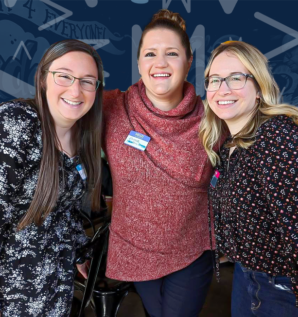 Three smiling women with glasses and name tags, standing close together with arms around each other.