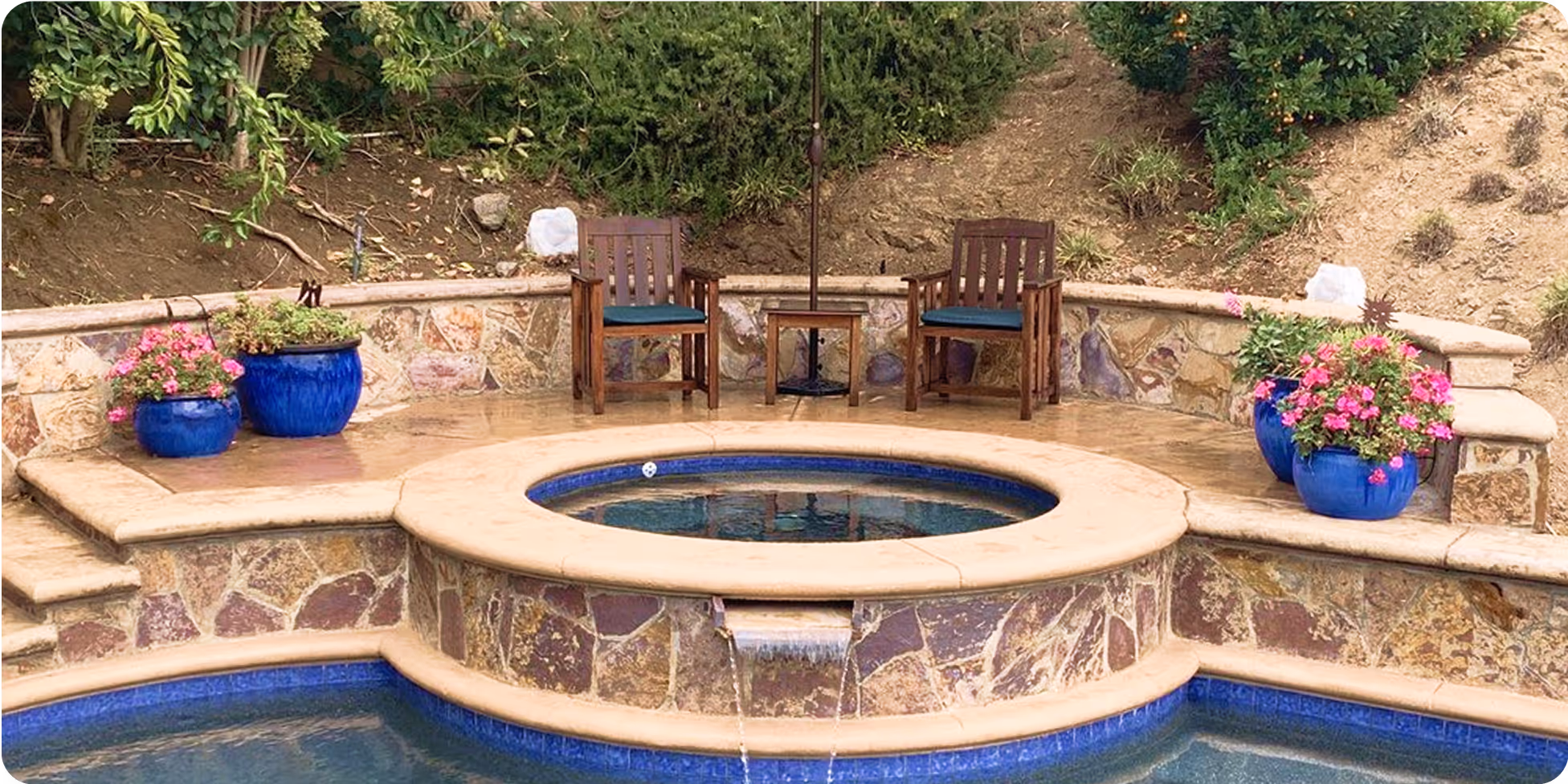 Stone patio with circular spa, wooden chairs, and blue flower pots