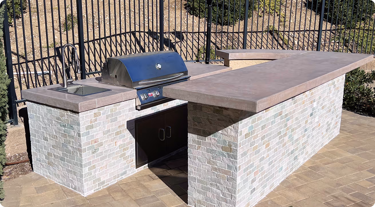 Outdoor kitchen with stone-clad island, grill, sink, and stone patio