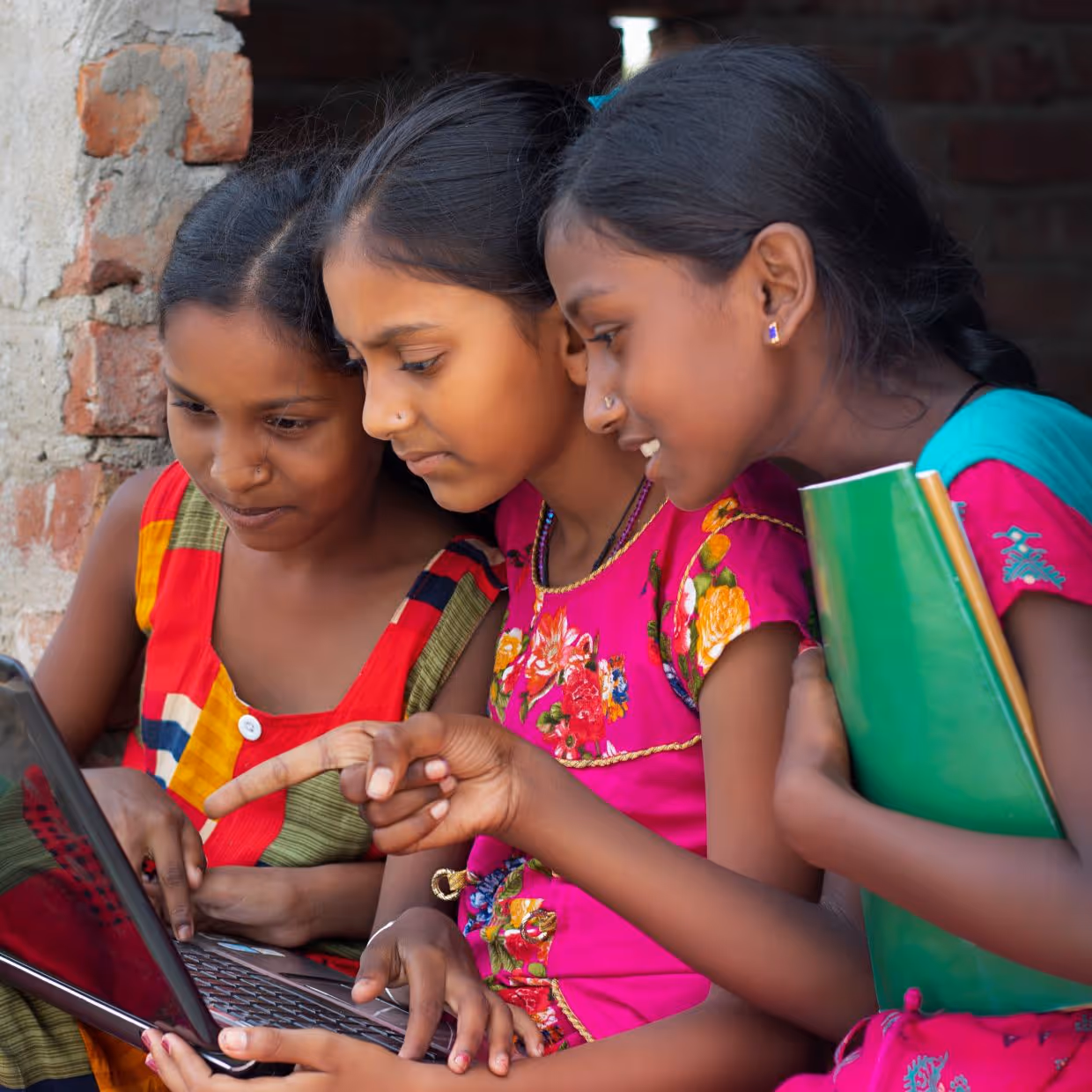 Three Indian school children looking at a laptop