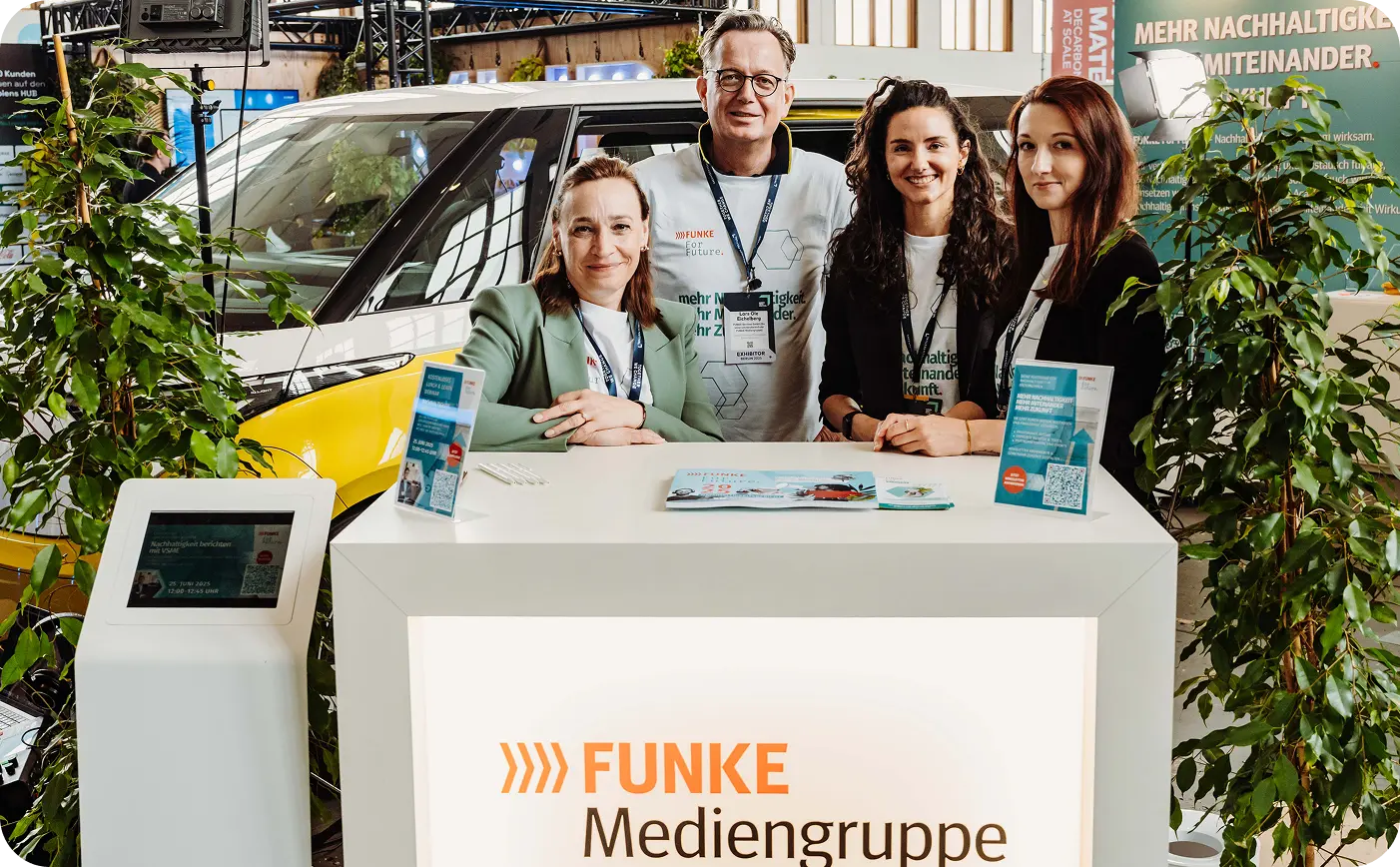 Vier Personen stehen an einem Messestand der FUNKE Mediengruppe mit grünem Elektroauto und Pflanzen im Hintergrund.