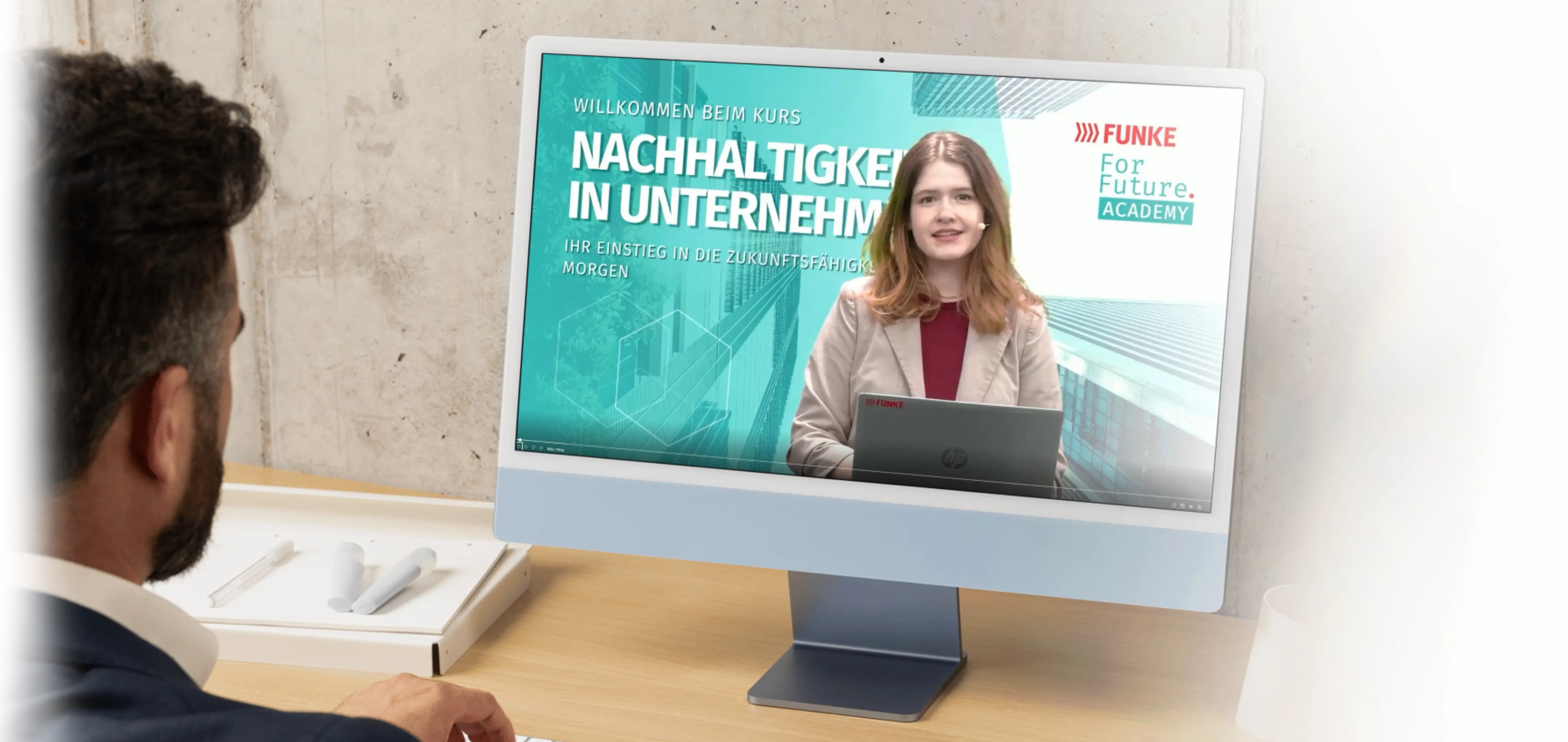 Ein Mann sieht sich an einem Schreibtisch einen Online-Kurs zum Thema Nachhaltigkeit in Unternehmen auf einem Desktop-Computer an.