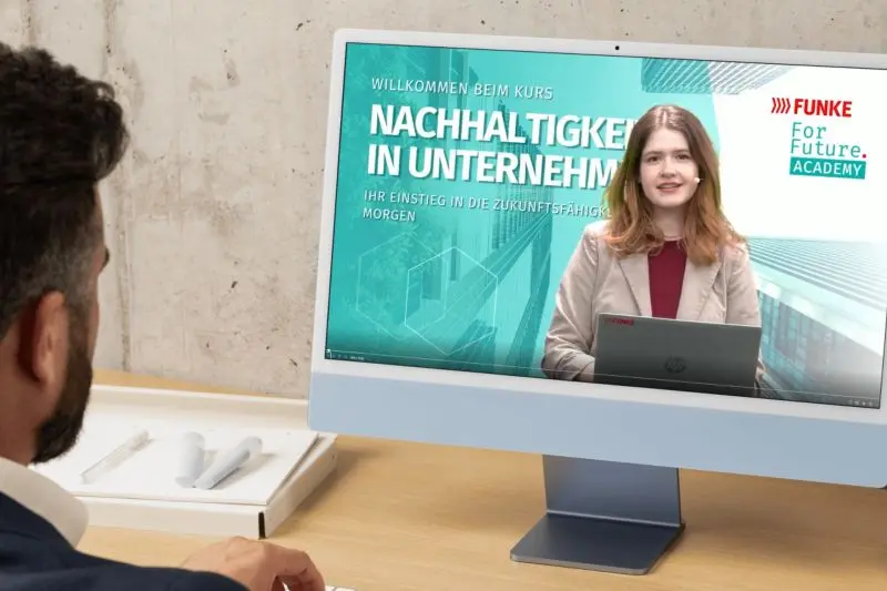 Ein Mann sieht sich an einem Schreibtisch einen Online-Kurs zum Thema Nachhaltigkeit in Unternehmen auf einem Desktop-Computer an.