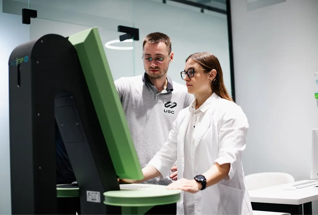 Лікар у білому халаті та фахівець-чоловік працюють разом за високотехнологічним діагностичним апаратом, підкреслюючи, що практична медицина та наука — нероздільні.