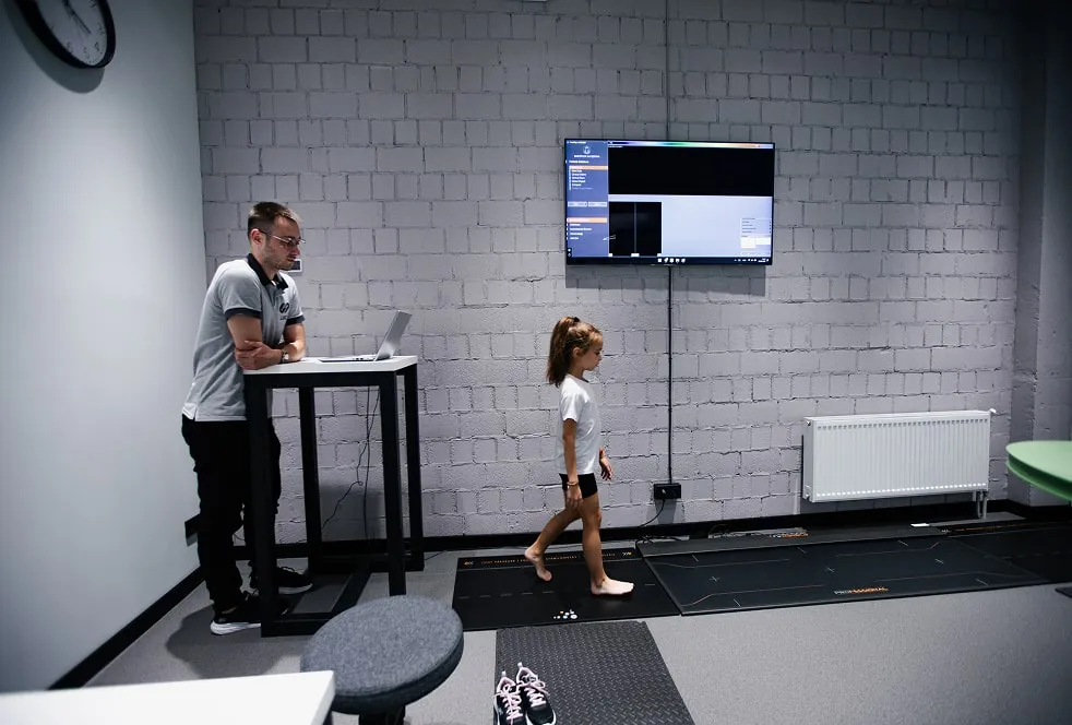 Чоловік-спеціаліст контролює ортодонтичний чекап дівчинки, яка йде по платформі аналізу ходи.