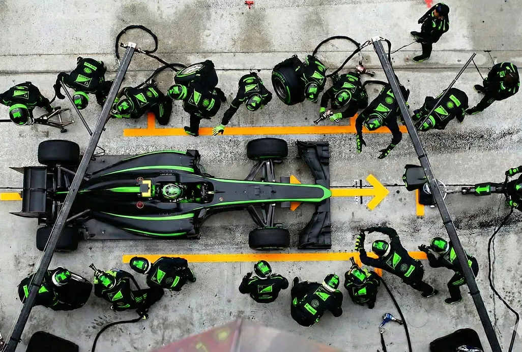 Зображення піт-стопу Формули-1. Чорно-зелений гоночний болід оточений командою механіків у відповідній уніформі. Вони працюють швидко й злагоджено, створюючи відчуття терміновості та командної роботи.