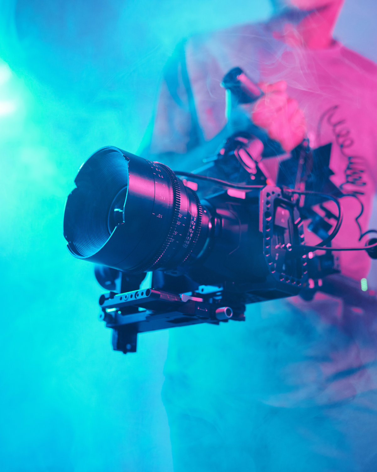 Caméra de cinéma professionnelle tenue par une personne dans une ambiance lumineuse bleue et rose avec de la fumée.