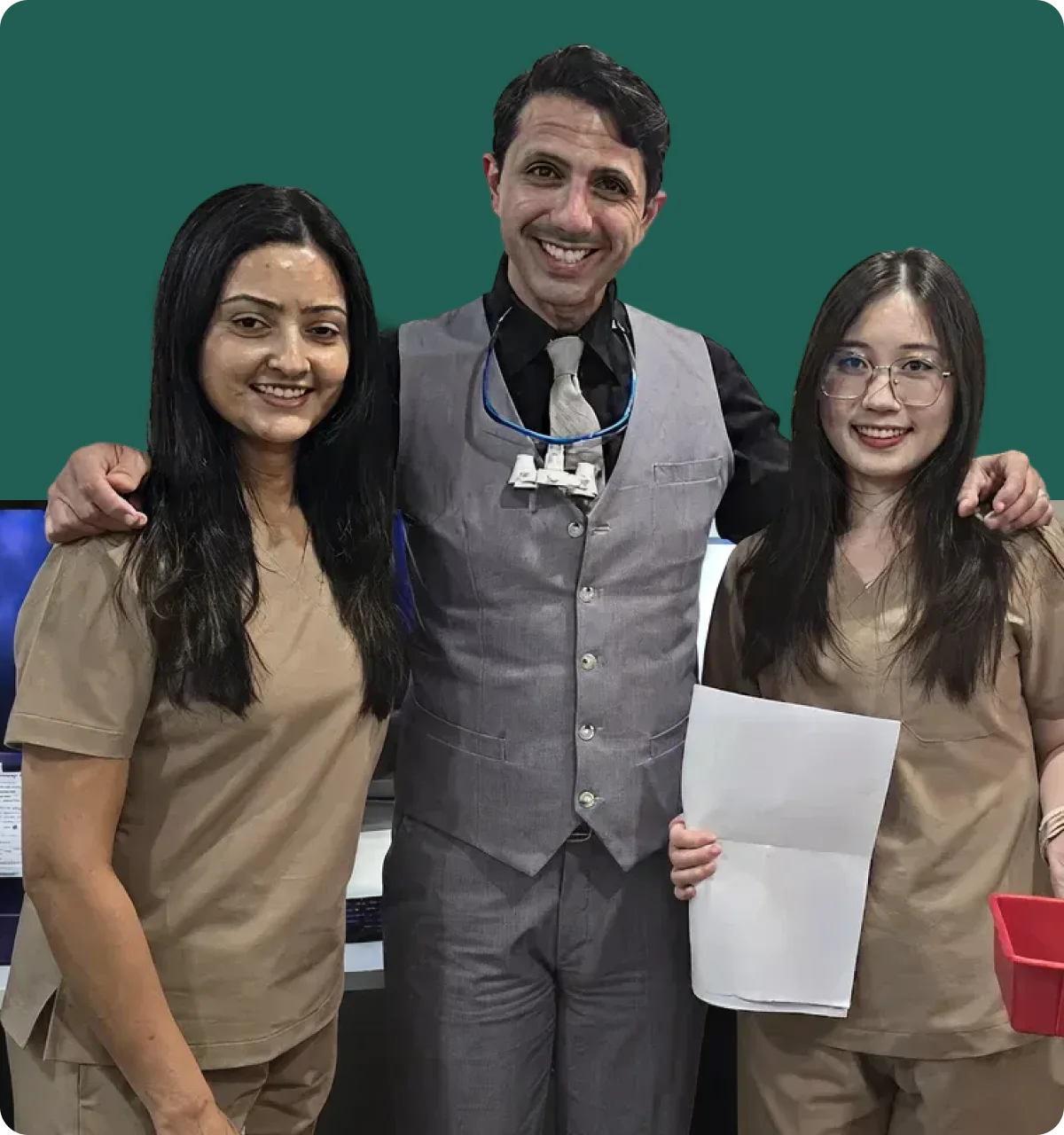 Dr. Sanad Al Murayati in a gray vest and tie stands with two women in beige scrubs, one holding papers and the other a red container.