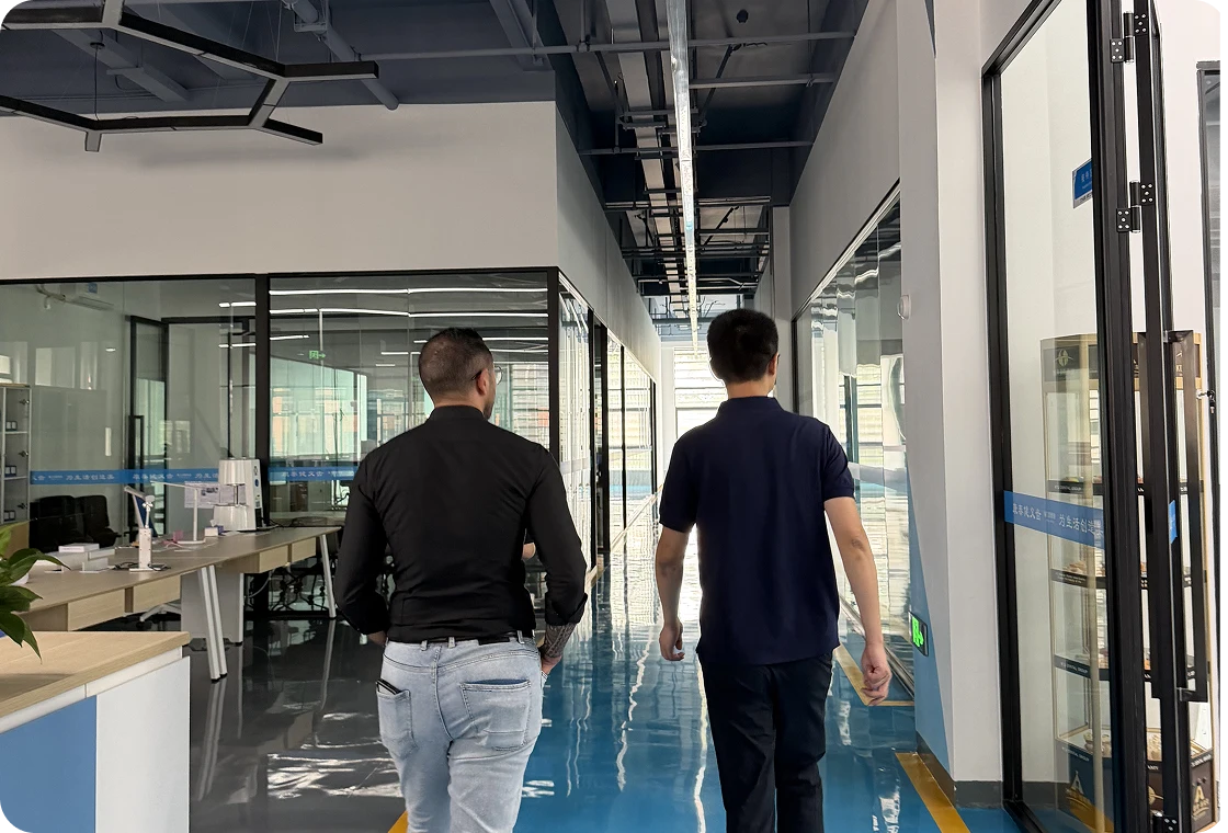 Two men walking down a shiny blue-floored office corridor with glass-walled rooms on either side.
