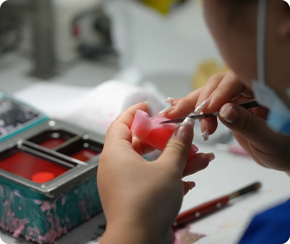 Person carefully sculpting pink dental mold using precision tool at a workbench.