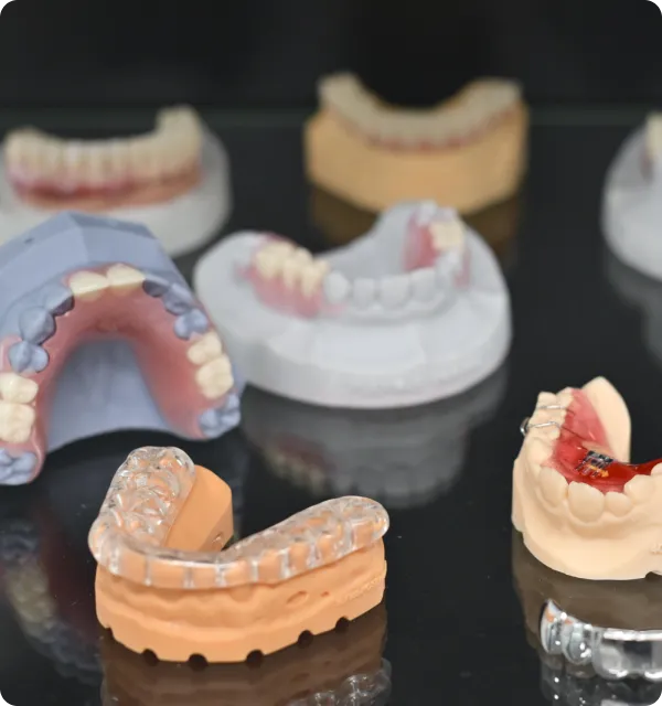 Dental molds displaying various orthodontic appliances, including clear aligners and braces models.