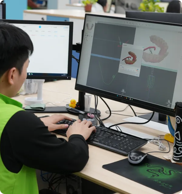 Person working on 3D modeling software on a dual-monitor computer setup in an office.
