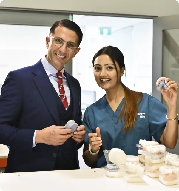 Two dental professionals smiling, holding dental models with more models on the table in front of them.
