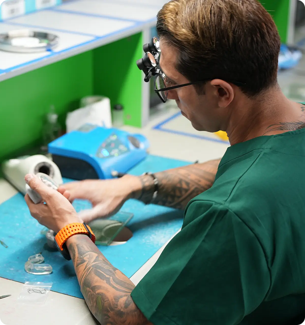 Man with magnifying glasses working at a lab bench on dental molds or prosthetics.