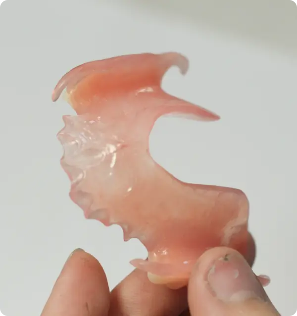 Hand holding a pink upper denture against a white background.