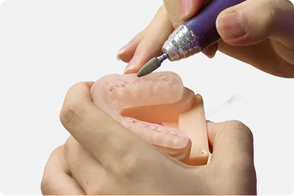 Hands holding a dental mold while a rotary tool polishes its surface.