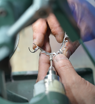 Close-up of hands crafting a metal dental partial denture using a rotary tool.