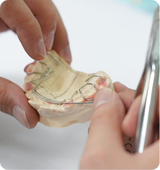 Hands holding and adjusting a clear dental retainer on a dental mold.