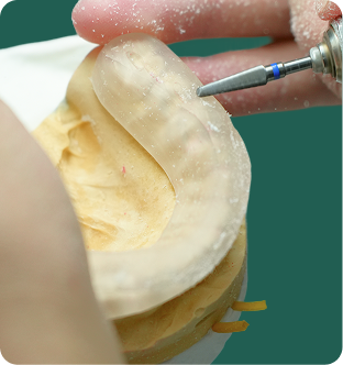 Close-up of dental technician shaping a teeth mold using a rotary tool.