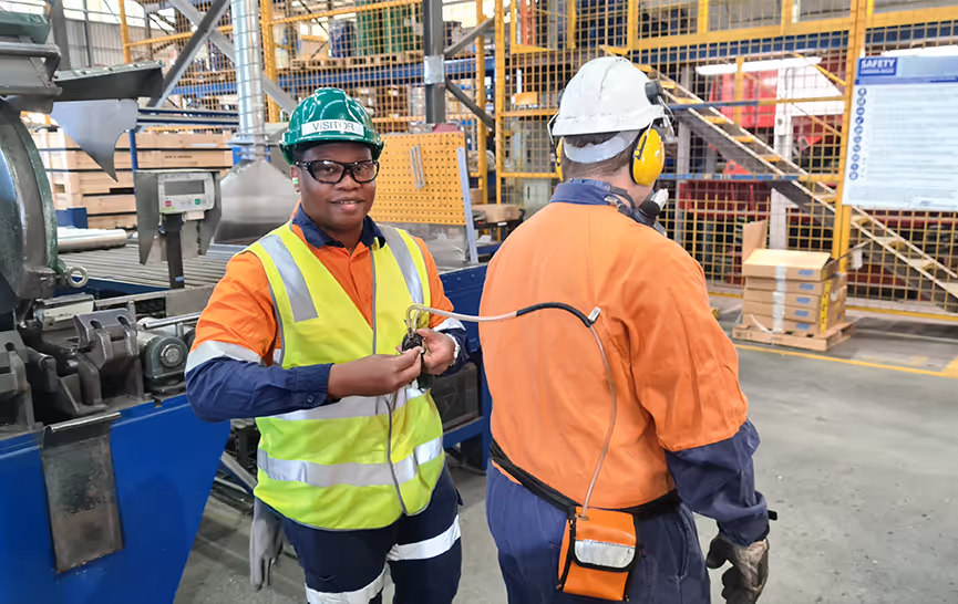 Two factory workers in safety gear connecting an air hose in an industrial setting.