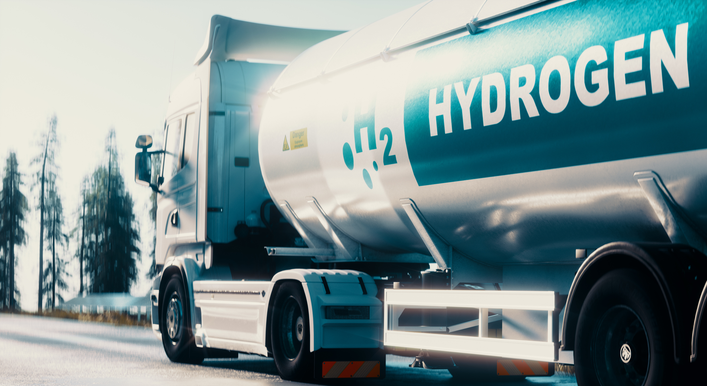 White tanker truck on a road carrying a tank labeled with H2 Hydrogen and a danger warning sign.