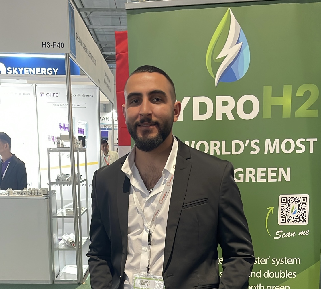 قبلان زاهوري يرتدي سترة سوداء وقميصاً أبيض ويقف أمام لافتة كشك هايدرو H2 خضراء في أحد المعارض.