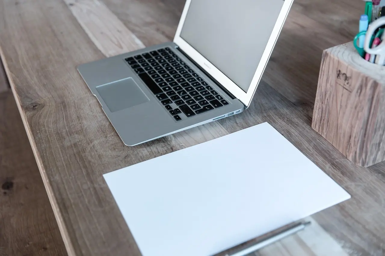 Minimalist wooden desk with an open laptop, blank sheet of paper, and a pencil holder — a clean workspace setup for productivity.